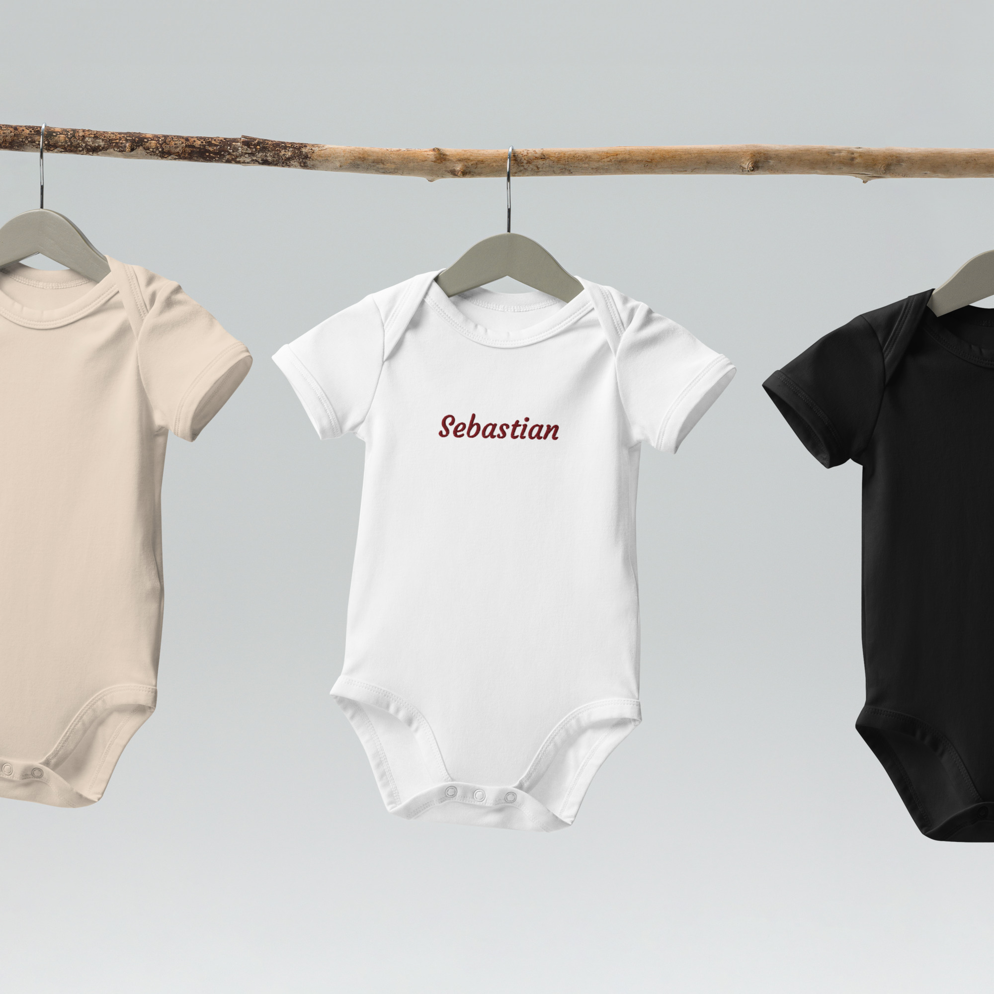 Personalised bodysuits in different colours hanging on branch